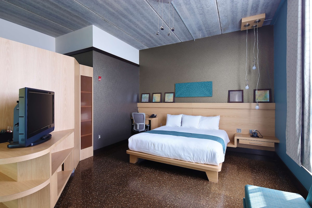 Een hotelkamer met een bed, nachtkastje, televisie en een bureau met stoel.
