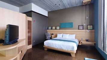 A hotel room with a bed, bedside table, TV, and a desk with a chair.