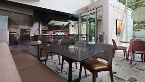 Een moderne eethoek met een grote tafel en stoelen, een keuken op de achtergrond, en een glazen wand met uitzicht op het landschap.