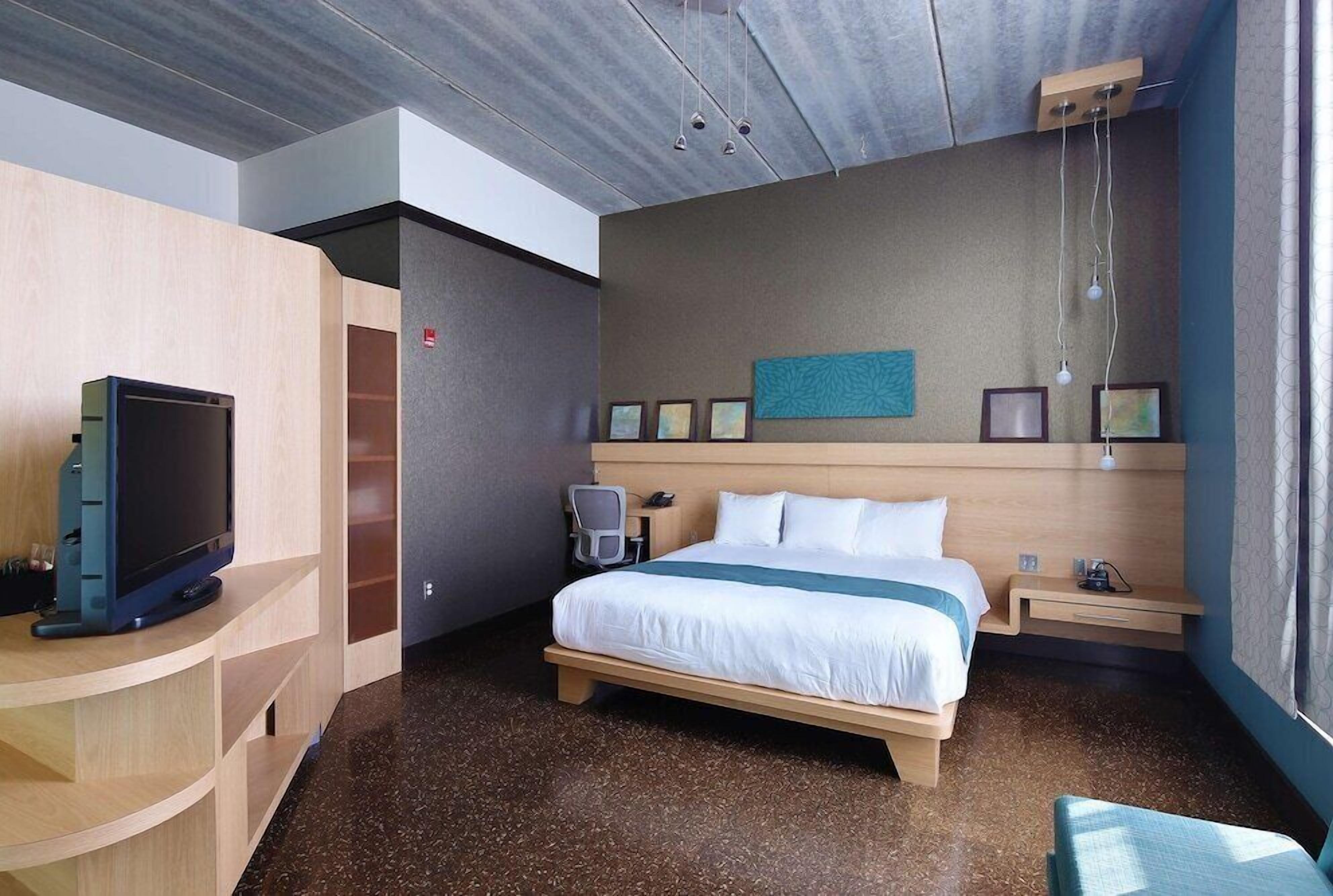 Een hotelkamer met een bed, nachtkastje, televisie en bureau met stoel.