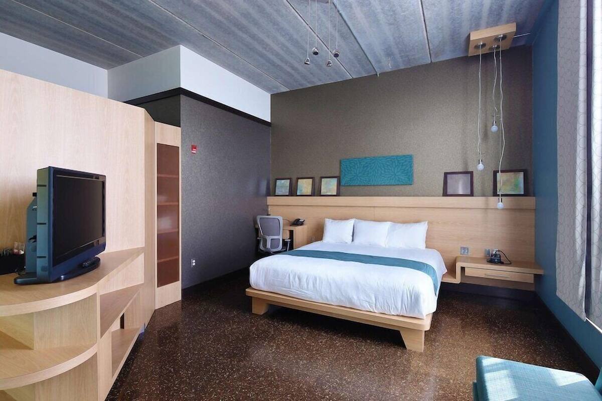 Een hotelkamer met een bed, nachtkastje, televisie en bureau met stoel.