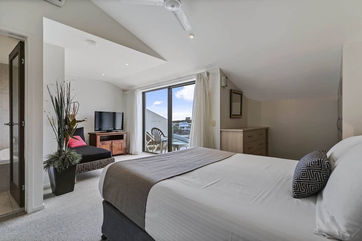 A modern bedroom with a large bed, a TV, a balcony, and a shower area.