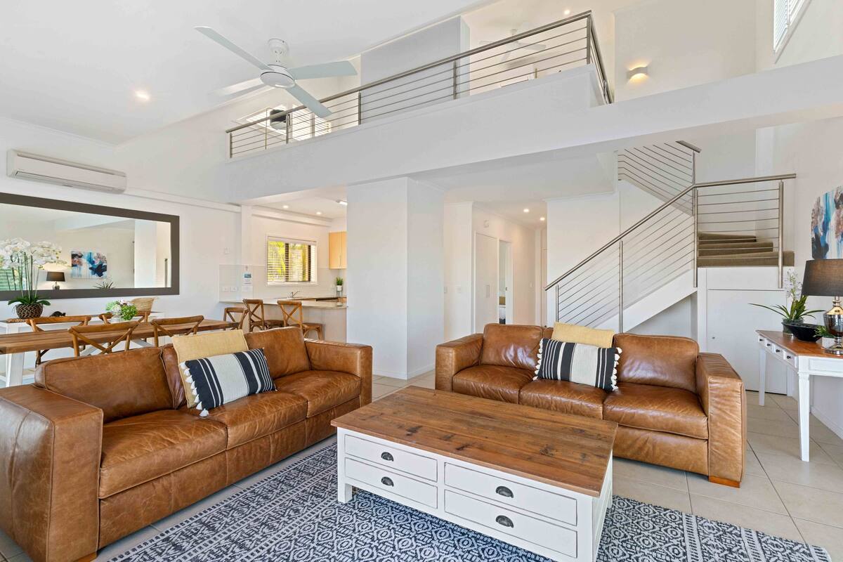 A spacious living area with two brown leather sofas, a wooden coffee table, and patterned rugs.