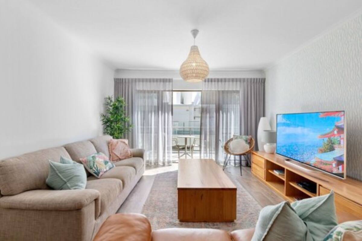 A modern living room with a sofa, coffee table, TV, and a dining area with a table and chairs.