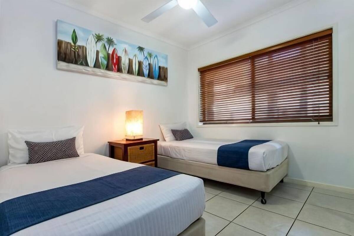 A bedroom with two beds, a painting, a nightstand, and a window with blinds.
