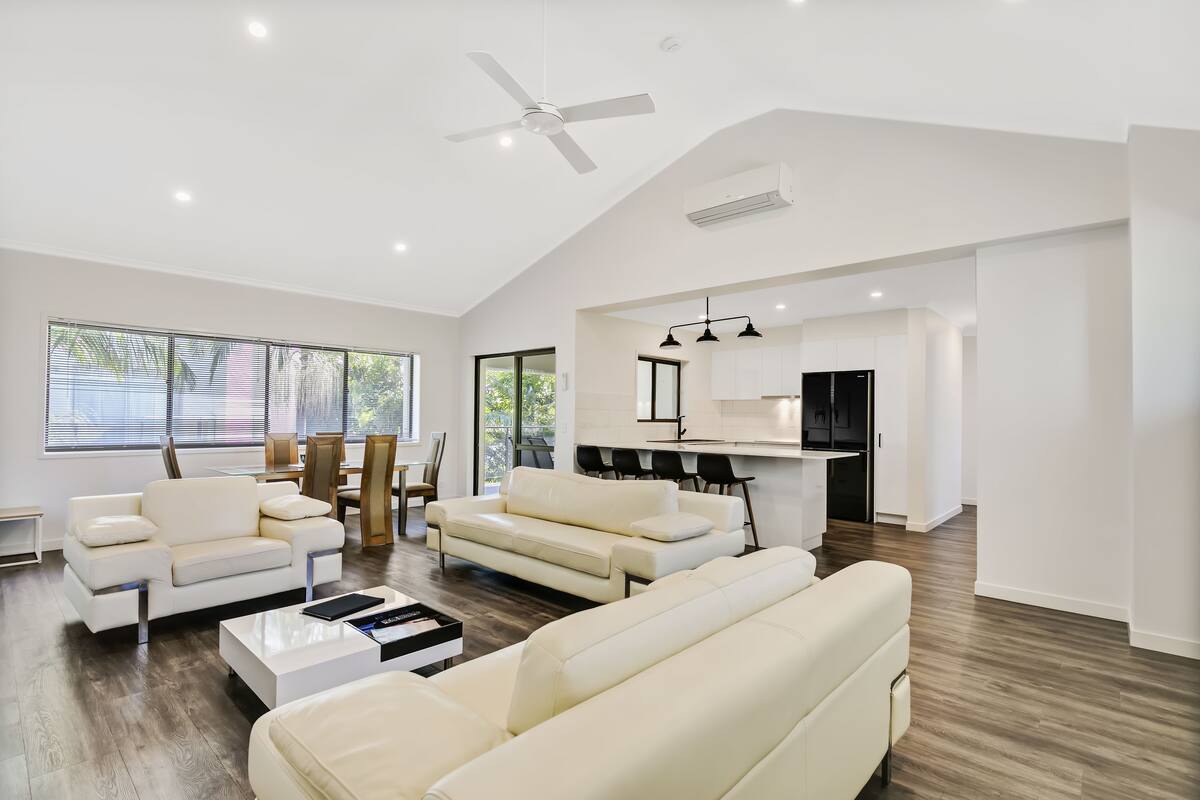 A spacious living area with a modern kitchen, white furniture, and large windows.
