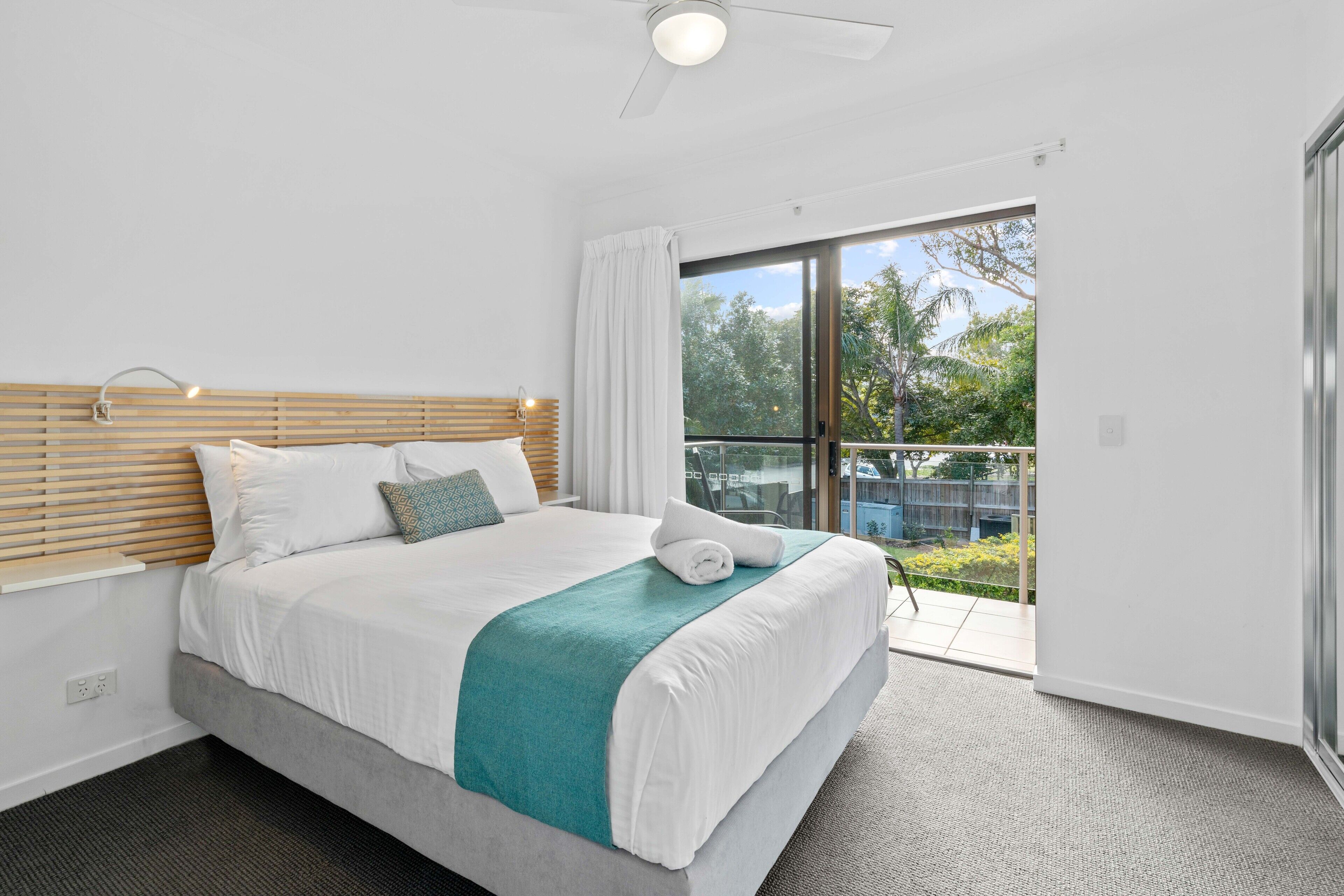 A modern hotel room with a large bed, a balcony with a glass door, and a ceiling fan.