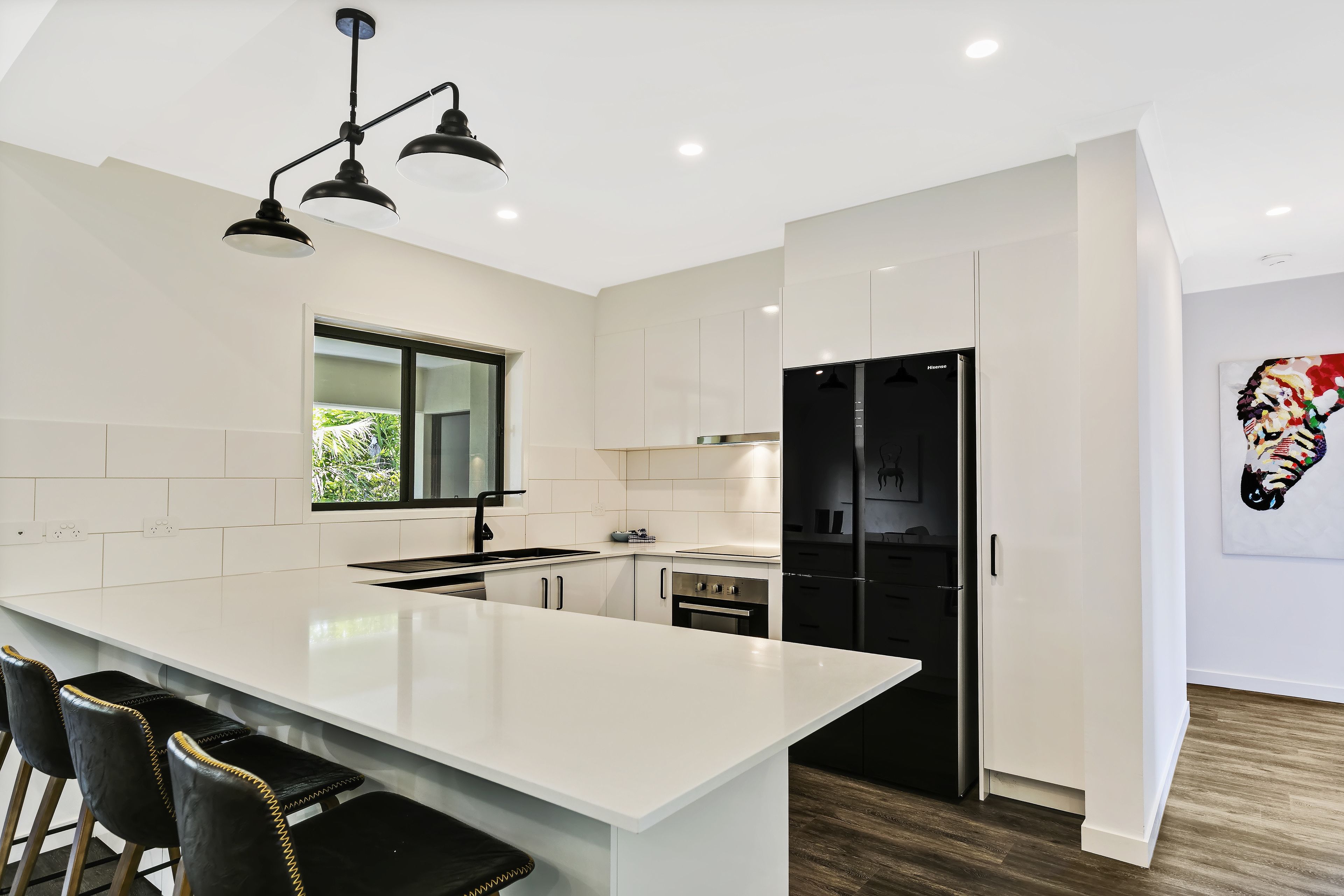 A modern kitchen with white cabinetry, a large island with bar stools, a black refrigerator, and a window providing natural light.