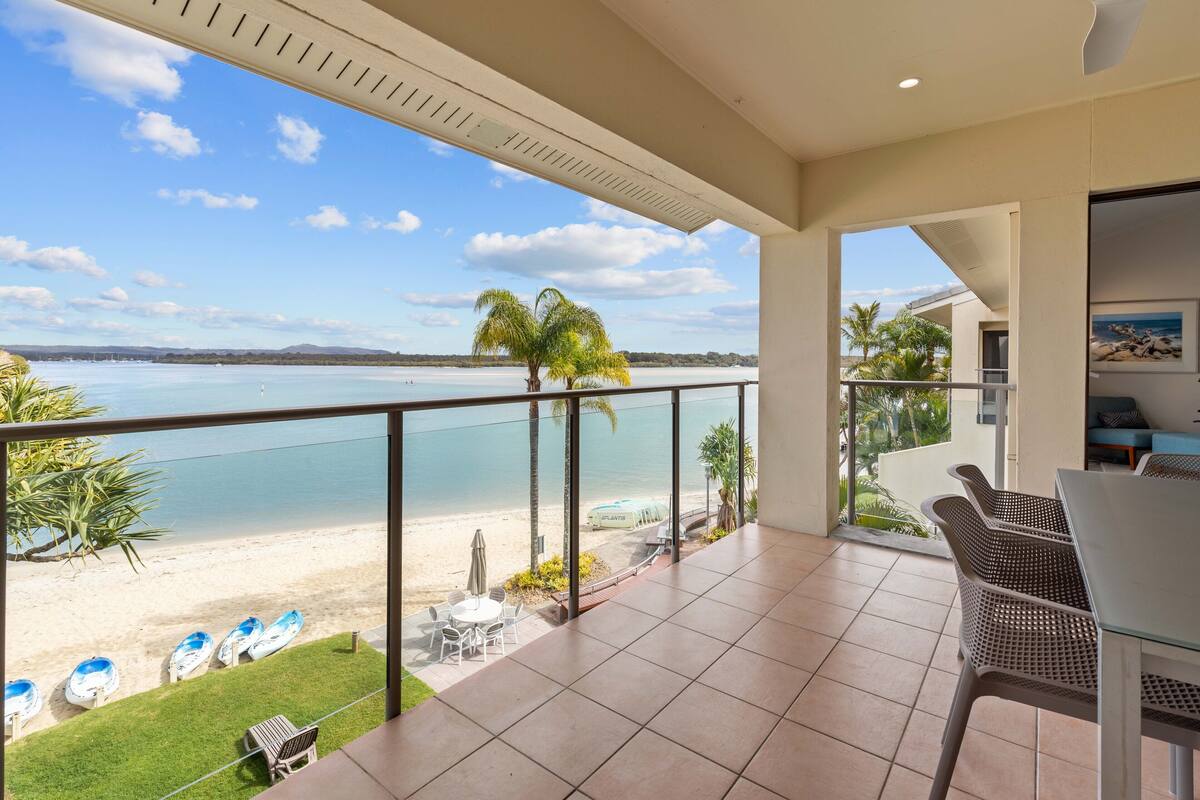 A balcony with a view of the beach and ocean, furnished with chairs and a table.