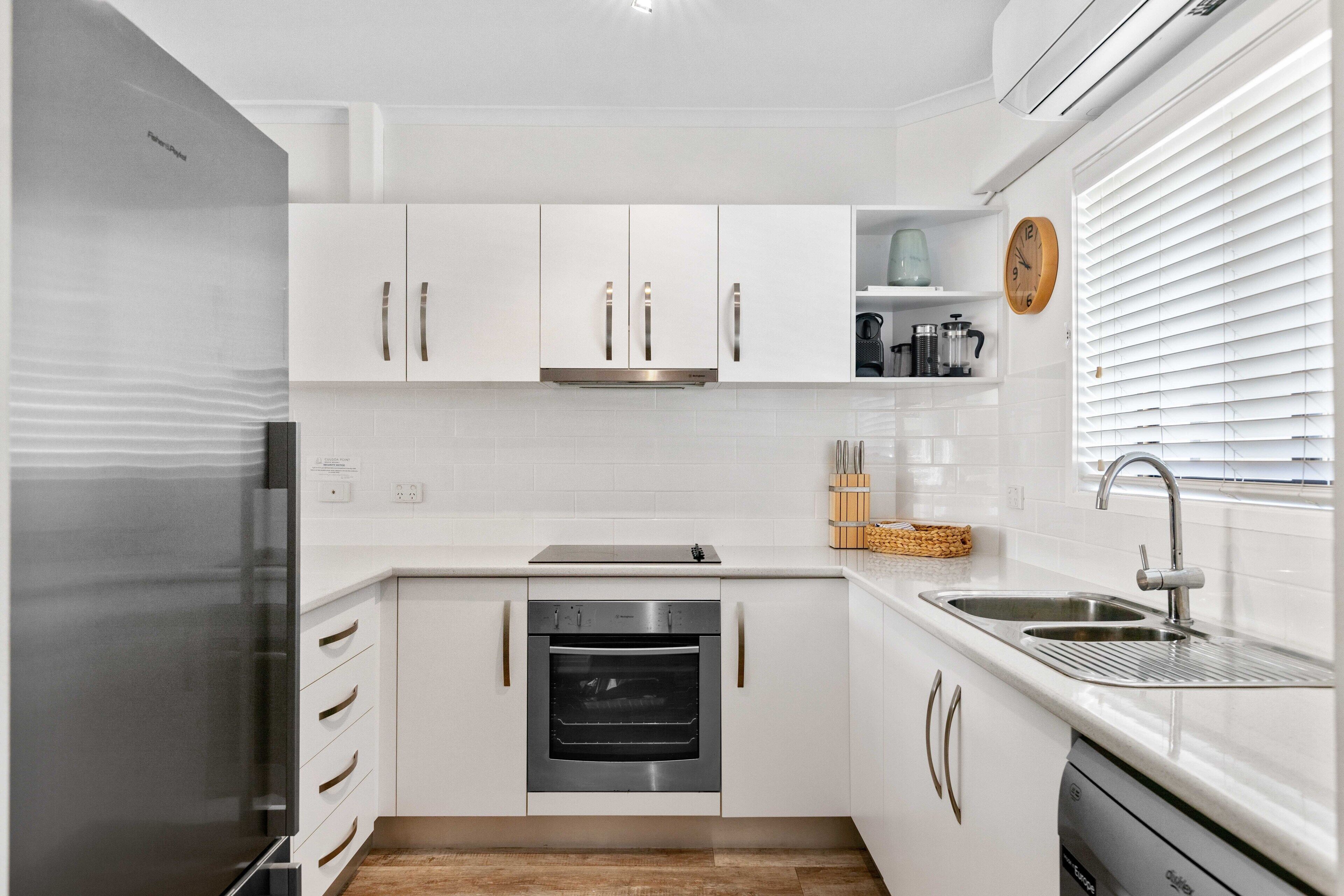A modern kitchen with white cabinets, a stainless steel refrigerator, an oven, and a sink with a faucet.