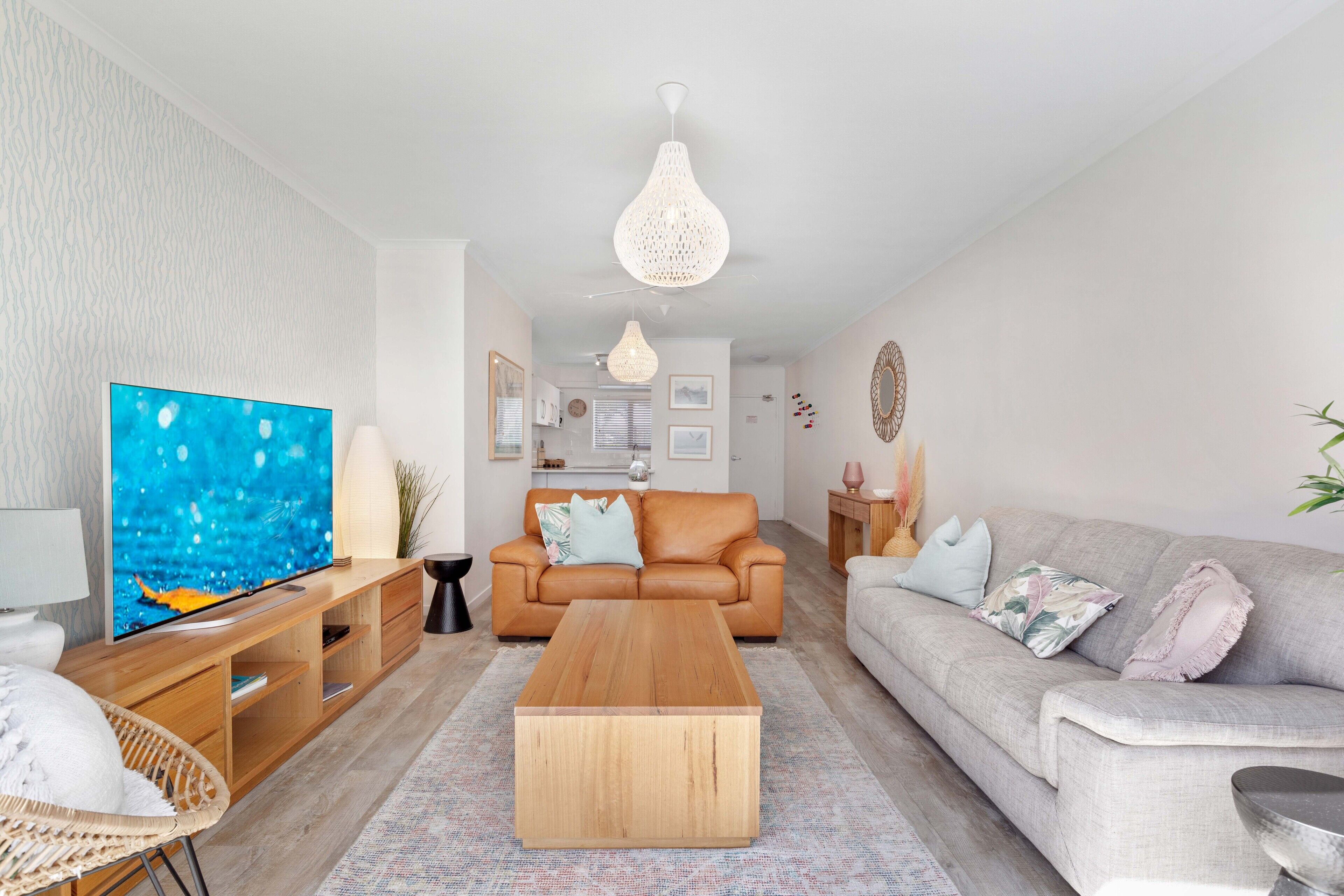 Ein modernes Wohnzimmer mit großem Flachbildfernseher, Couchtisch aus Holz, Ledersofa und einem gemusterten Teppich.