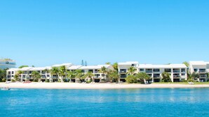 Un hotel frente a la playa con varias edificaciones, una playa de arena y un cielo azul despejado.