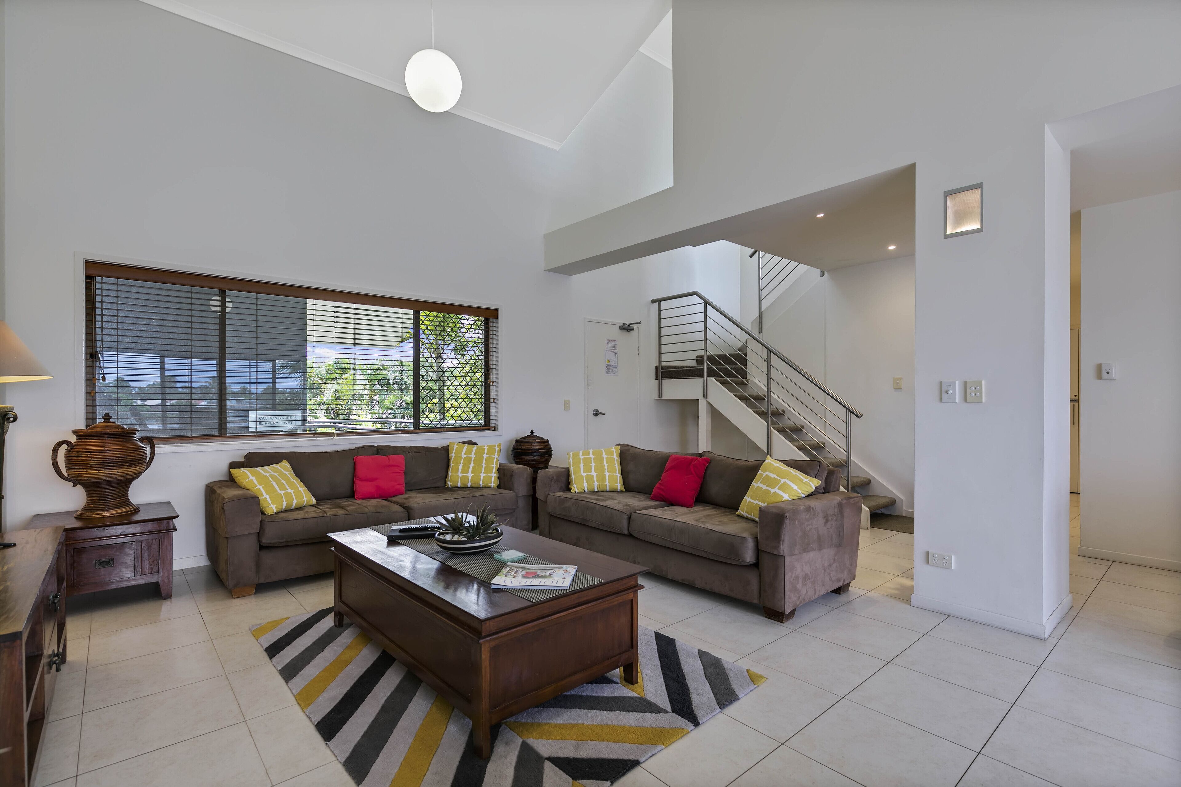 A spacious living room with a large window, a staircase, and a modern kitchen area.