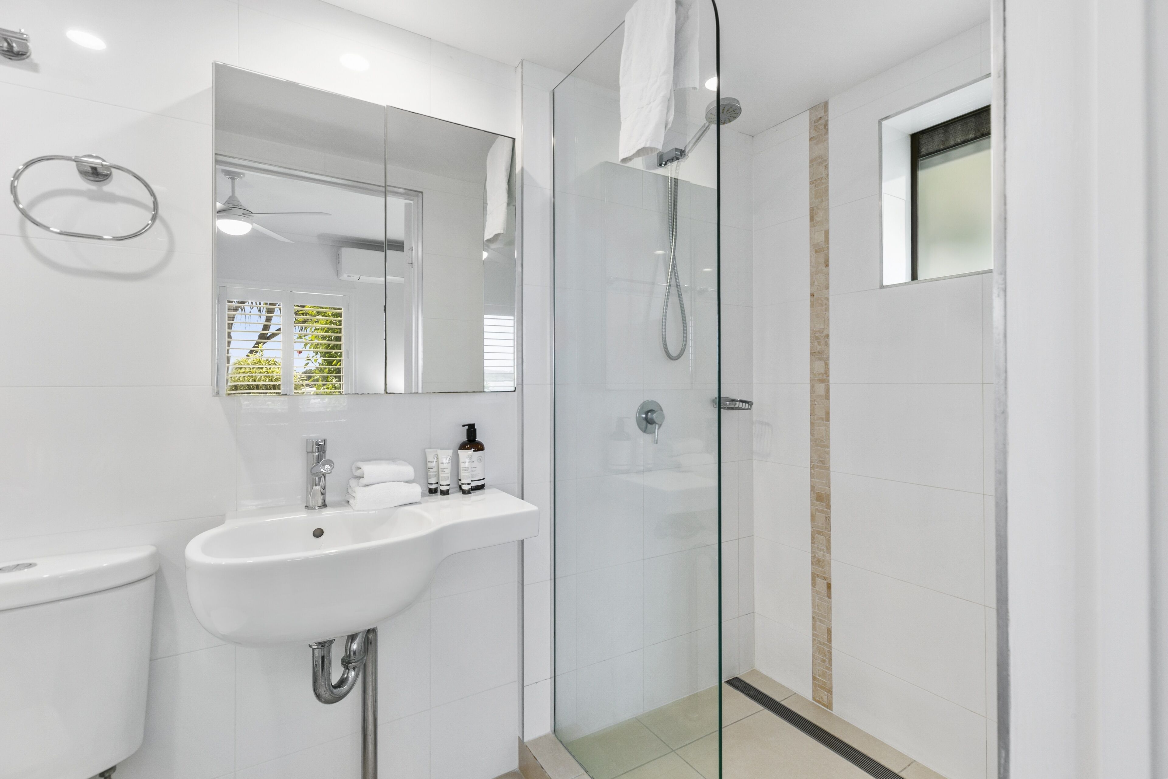 Un baño moderno con ducha envuelta en vidrio, un lavamanos con artículos de aseo y un espejo.