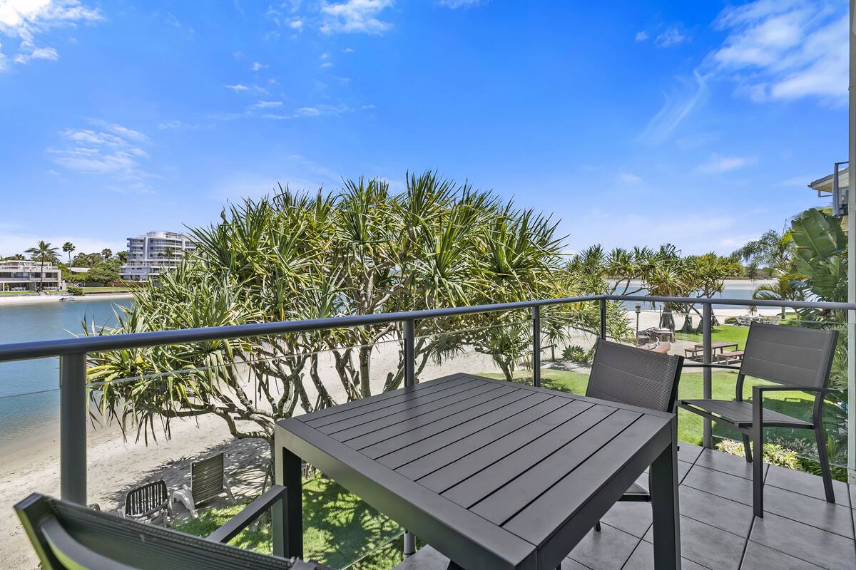 A balcony with a table and chairs, overlooking a beach and palm trees.