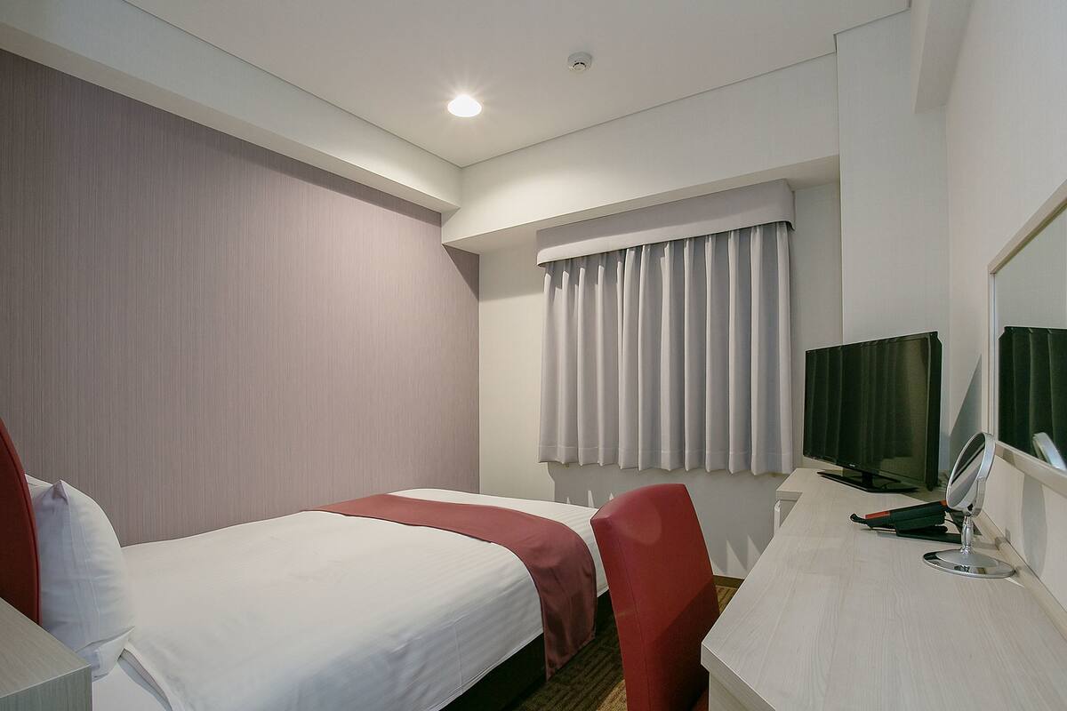 Ein Hotelzimmer mit zwei Betten, einem Schreibtisch, einem Fernseher und einem Spiegel.