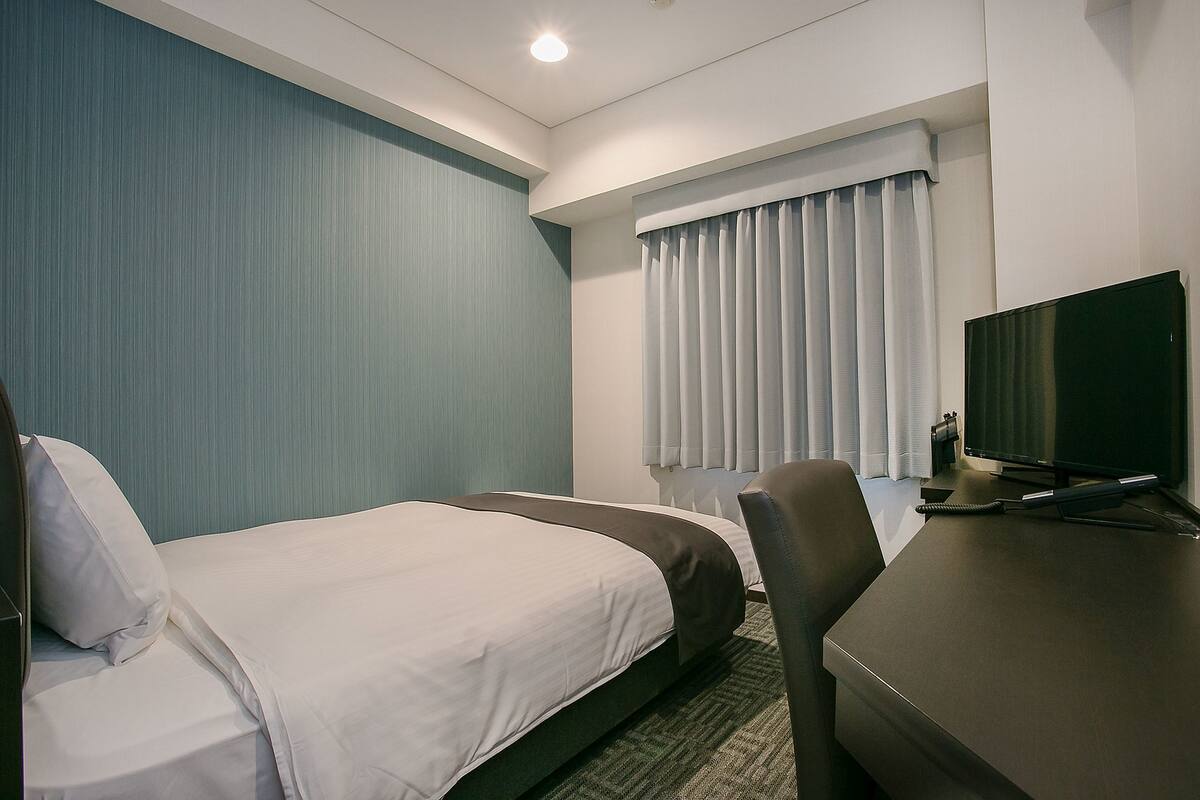 Ein Hotelzimmer mit zwei Betten, einem Schreibtisch, einem Fernseher und einem Fenster mit Vorhängen.