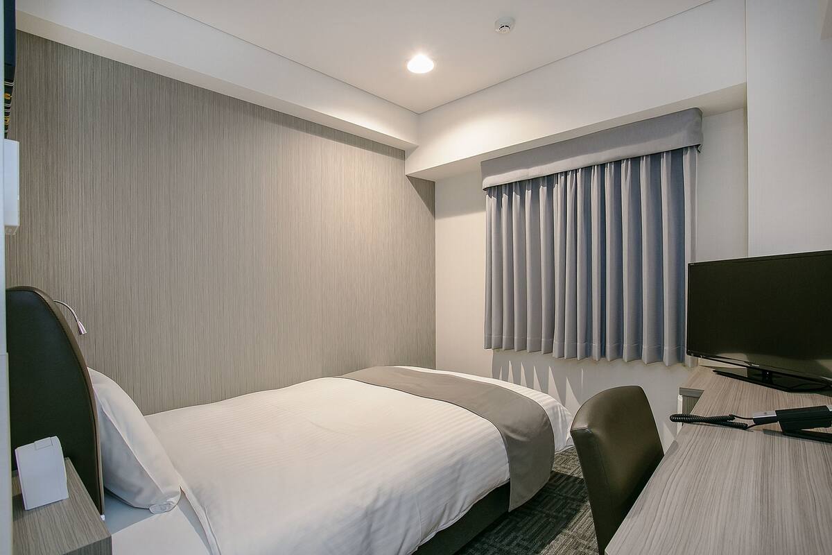 Ein Hotelzimmer mit zwei Betten, einem Schreibtisch, einem Stuhl und einem Fernseher.