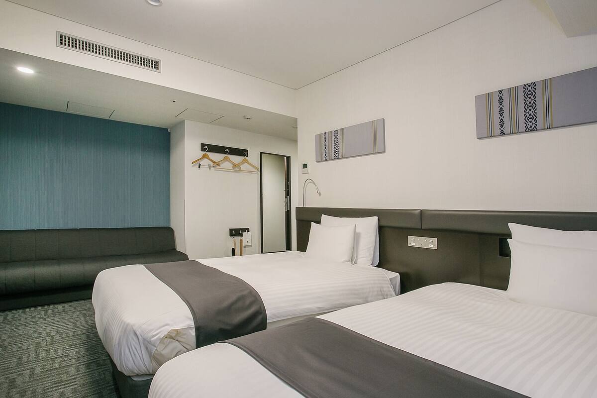Ein Hotelzimmer mit zwei Betten, einer blauen Akzentwand und einem Spiegel.