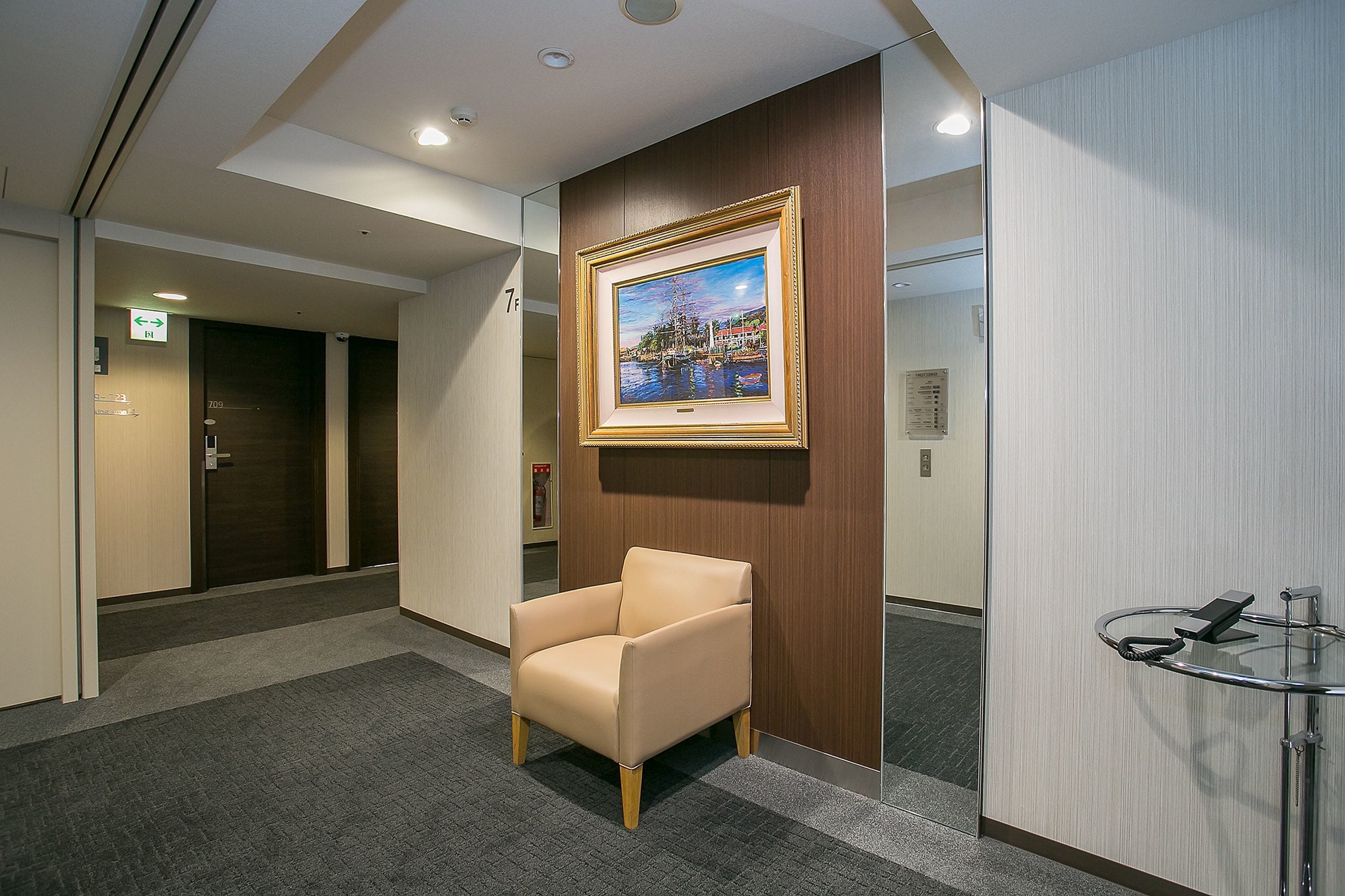 Un vestíbulo de hotel con un cuadro enmarcado, un sillón color beige y una mesa de vidrio.