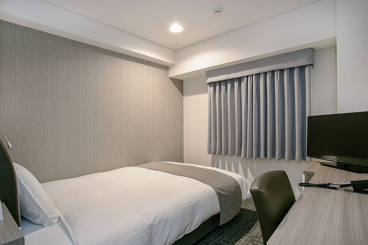 Ein Hotelzimmer mit zwei Betten, einem Schreibtisch, einem Sessel, einem Fernseher und einem Fenster mit Vorhängen.