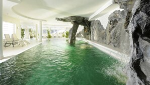 An indoor swimming pool with a natural rock formation, lounge chairs, and a modern ceiling design.