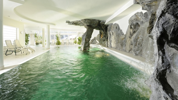 Ein Innenpool mit einer natürlichen Felsformation, Liegestühlen und einem modernen Deckenbau.
