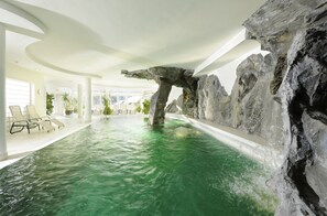 Une piscine intérieure agrémentée d’une formation rocheuse naturelle, de chaises longues et d’un design de plafond moderne.