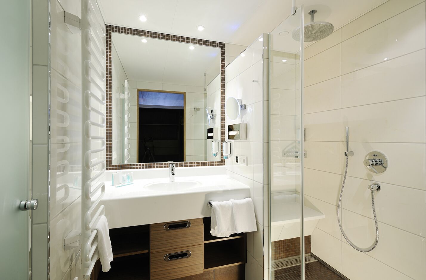 A modern bathroom with a white sink, a large mirror, and a glass-enclosed shower.