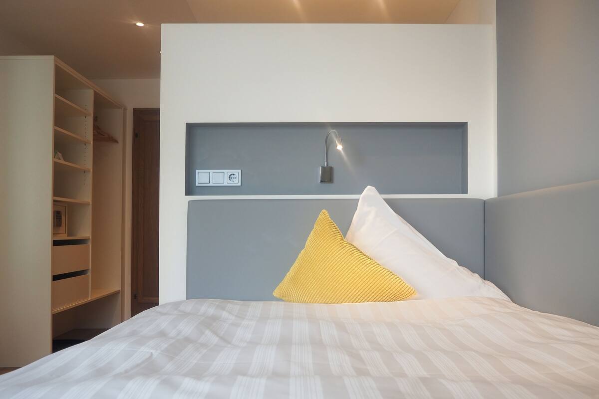 Un dormitorio con cama, mesita de noche, luz empotrada en la pared y armario integrado.