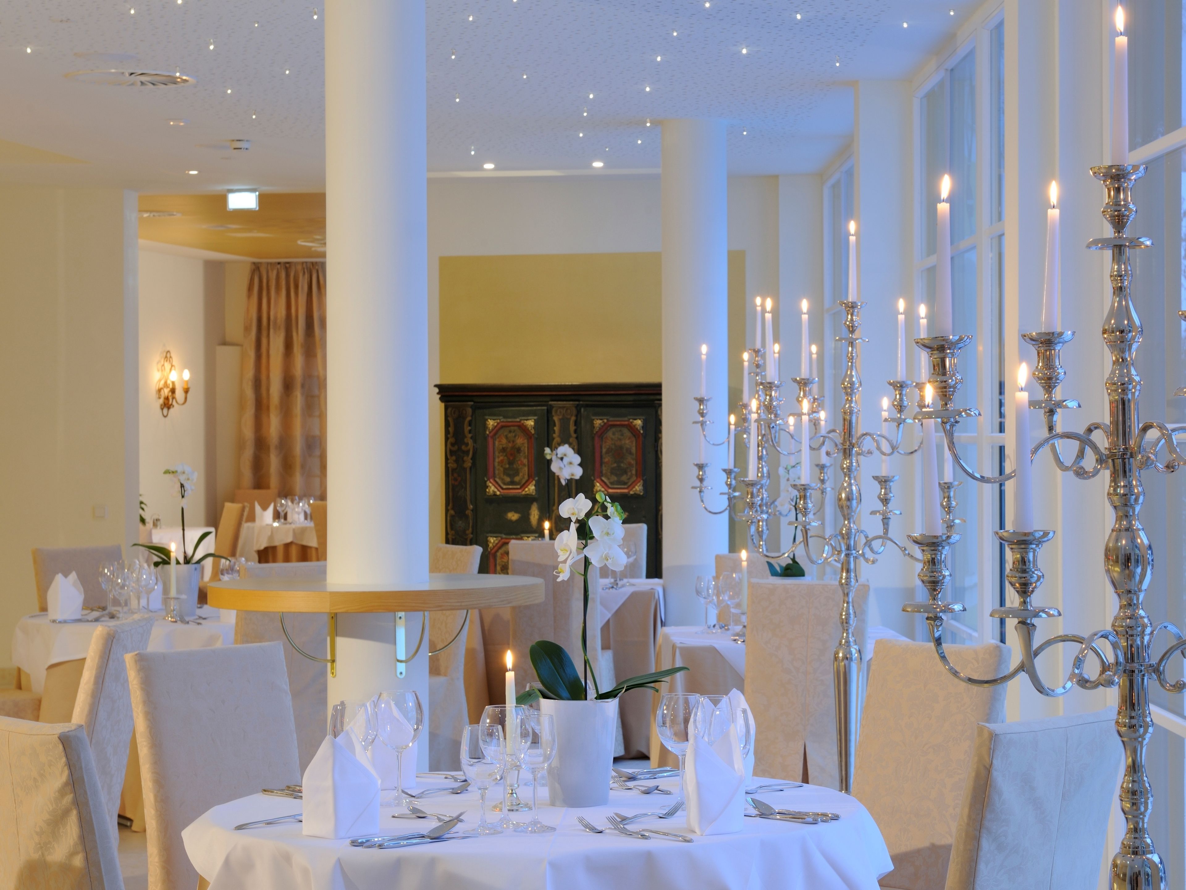 A formal dining room with white tablecloths, silverware, and candle-lit candelabras.