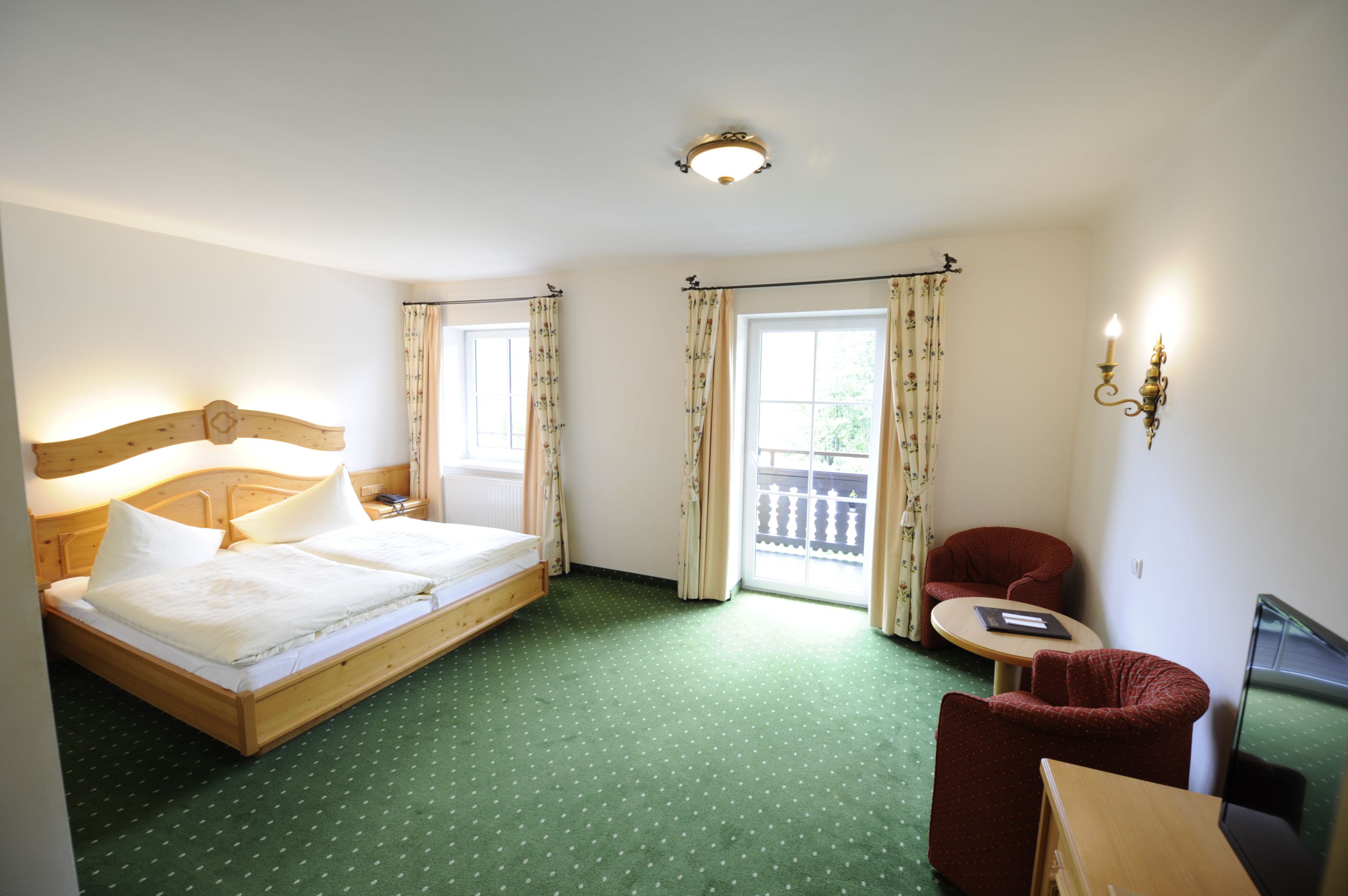 Een hotelkamer met een bed, een stoel, een klein tafeltje en een raam met gordijnen.