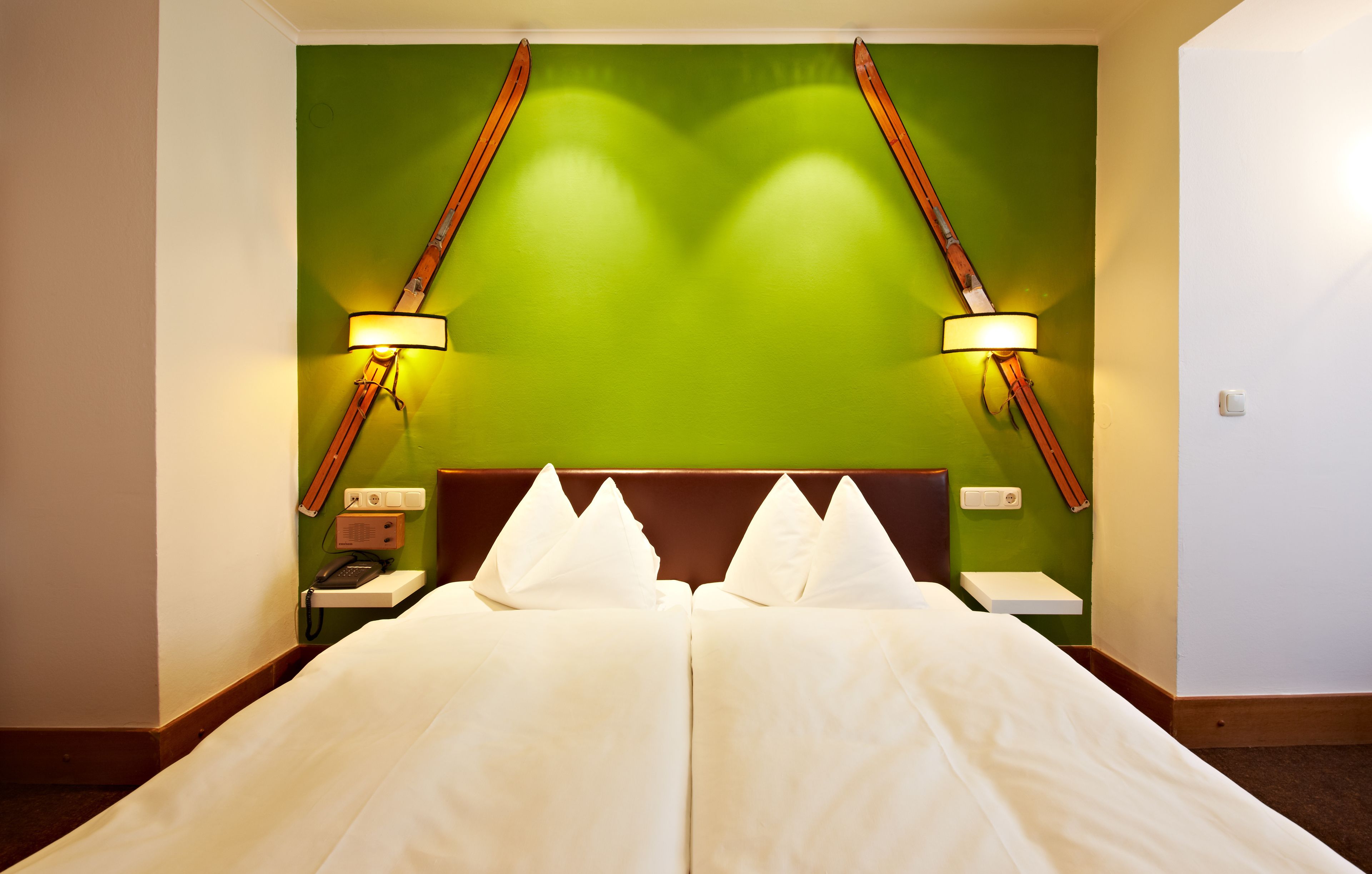 A hotel room with a large bed, green accent wall, and two bedside lamps.
