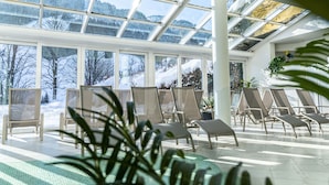 Ein Wintergarten mit großen Fenstern, Lounge-Möbeln und Zimmerpflanzen.