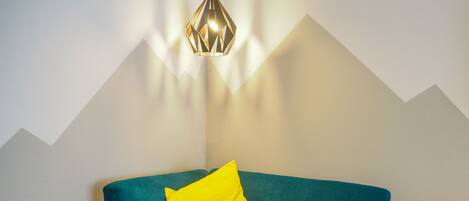 A teal sofa with a yellow pillow against a white wall with a geometric pattern.
