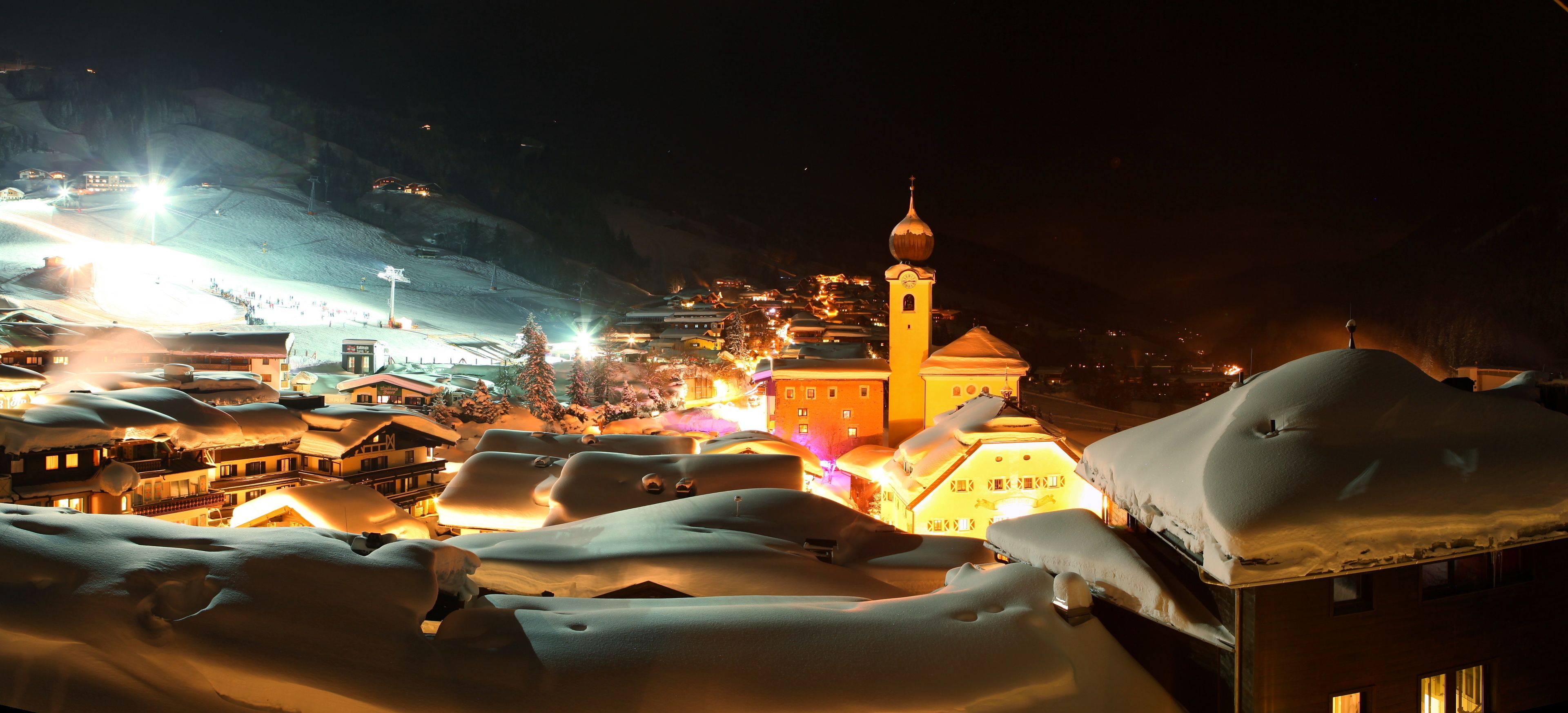 A snow-covered town at night with illuminated buildings and a prominent church tower.