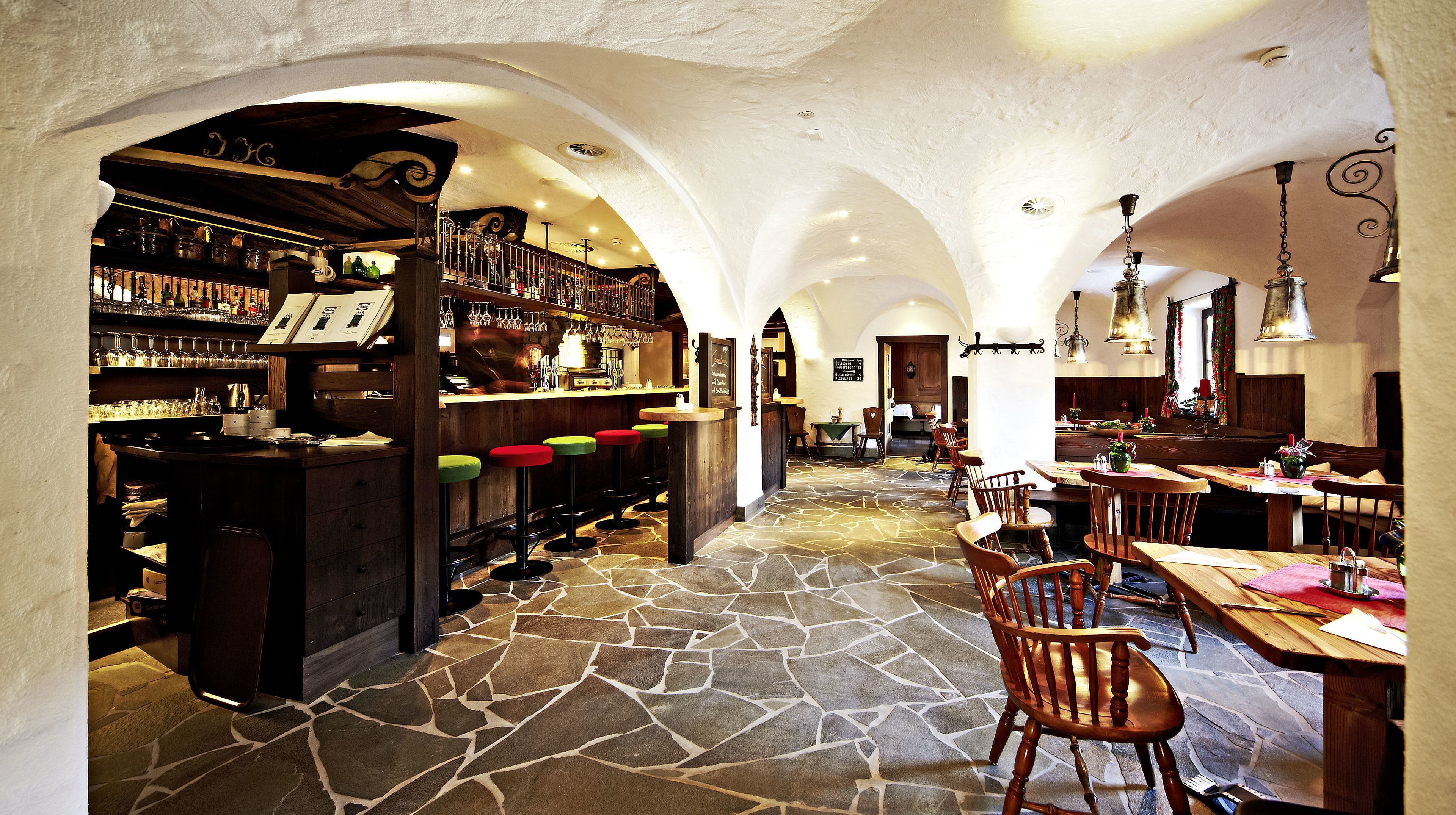 A bar area with stools, a counter with bottles, and a dining area with tables and chairs.