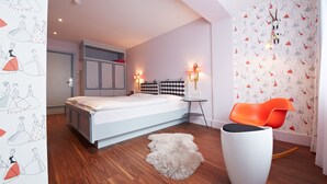 A modern bedroom with a large bed, a small table, a chair, and a rug.