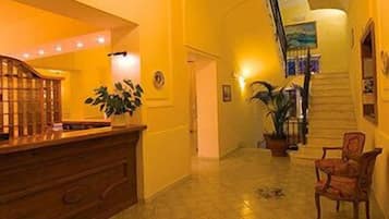 A hotel lobby with a reception desk, a staircase, and a chair.