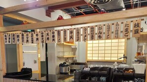 A restaurant interior with a wooden counter, menu boards with Japanese text, and a traditional sliding door. - Oasis Hotel Kuwait (Kuwait City)