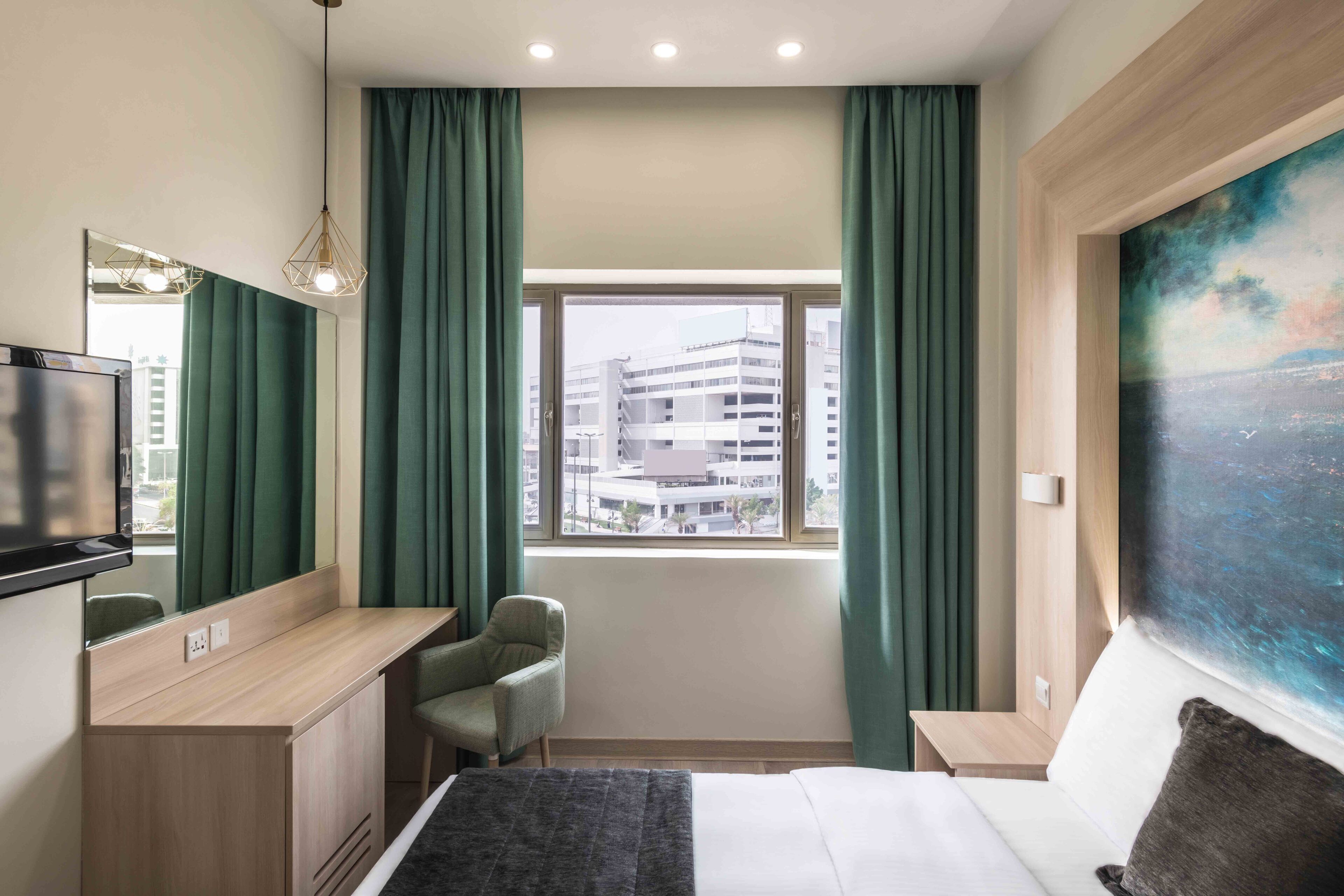 Una habitación de hotel con cama, escritorio, silla, televisor, ventana con cortinas y un cuadro en la pared.