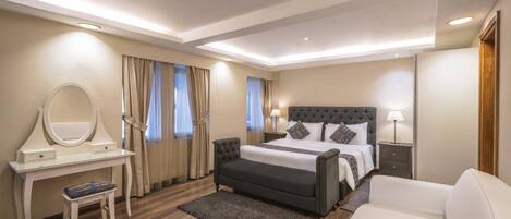 A modern bedroom with a large bed, a bedside table with a lamp, a vanity with a mirror, and a small stool.