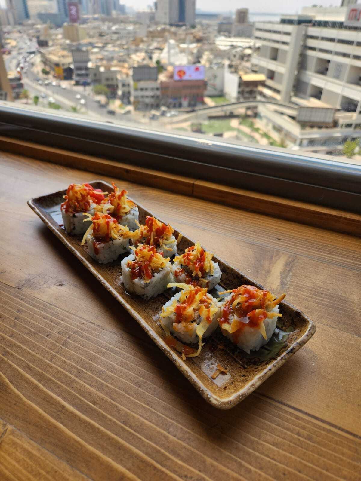 Un plato de sushi sobre una vajilla de cerámica, con vista a la ciudad a través de una ventana.