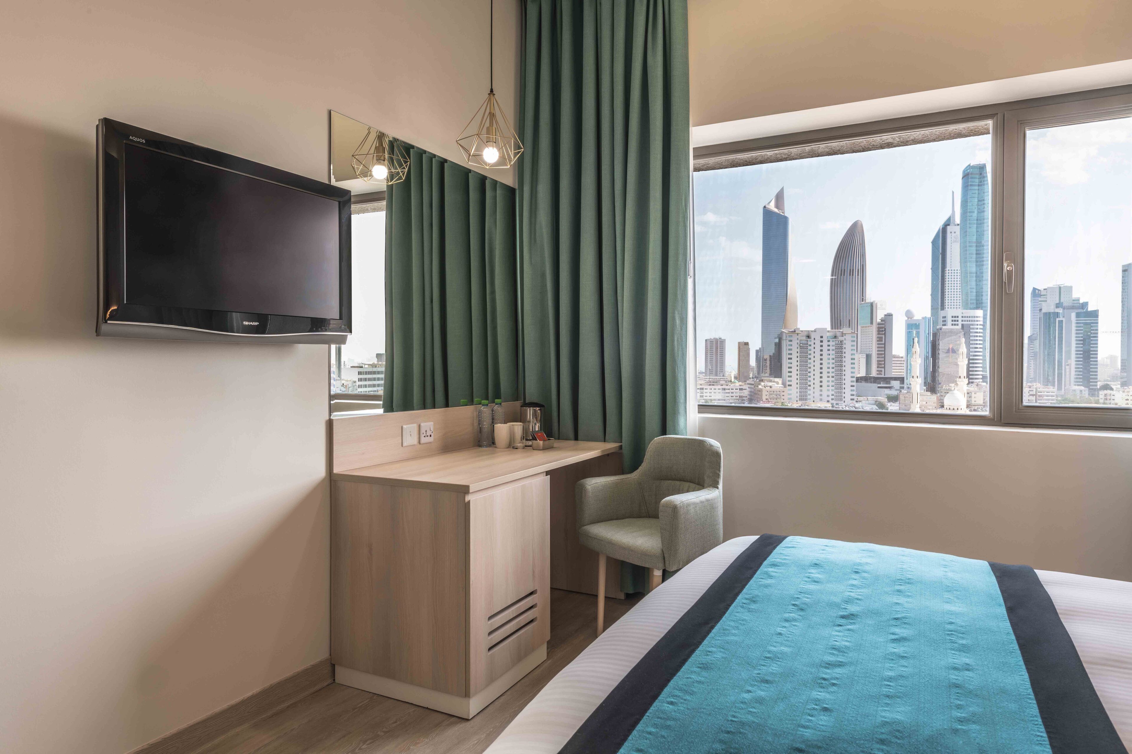 Una habitación de hotel con cama, escritorio, silla, televisor y ventana con vista a la ciudad.