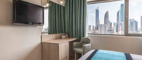 A hotel room with a bed, a desk, a chair, a TV, and a window with a cityscape view.