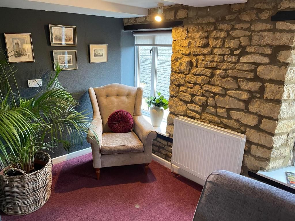 A cozy room with a stone wall, a window with blinds, a radiator, a cushioned armchair, a potted plant, and framed pictures on the wall.