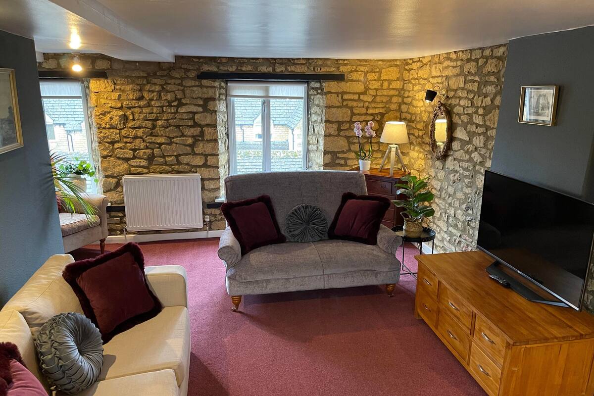 A cozy living room with a stone wall, a grey sofa, a white sofa, a wooden cabinet, and a flat-screen TV.