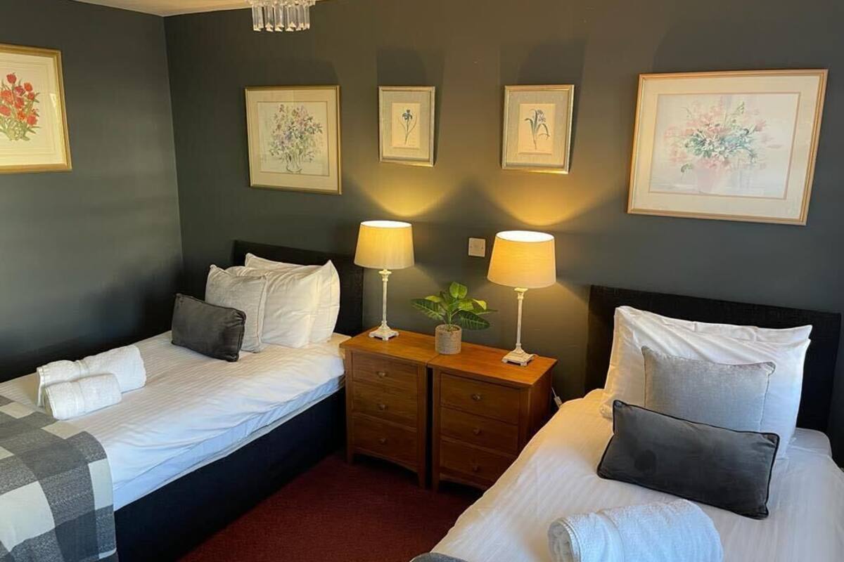 A hotel room with two beds, a nightstand with lamps, and framed floral artwork on the walls.