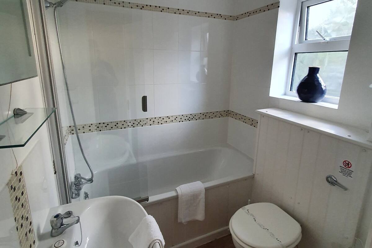 A bathroom with a bathtub, toilet, sink, and a window with a vase.