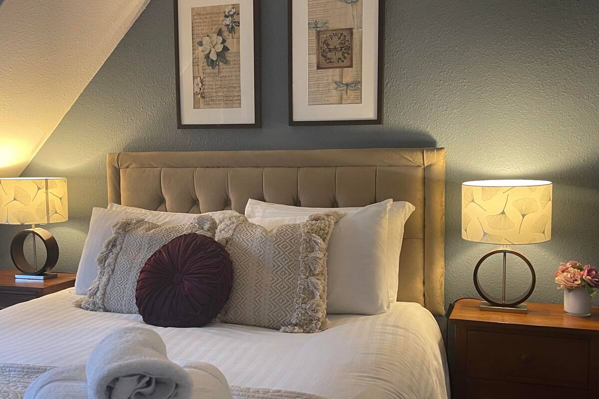 A well-appointed bedroom with a tufted headboard, a neatly made bed with multiple pillows, and two wall-mounted lamps on either side.